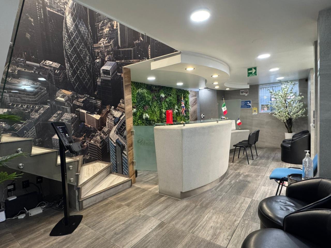 Recepción remodelada Universal House vista completa: mural Londres, escalera, muro verde y área de espera